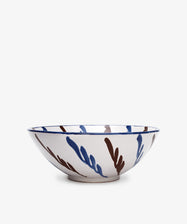 The Rayas Serving Bowl is a shallow, round ceramic piece with a white base and abstract blue and brown brushstroke patterns on its exterior.