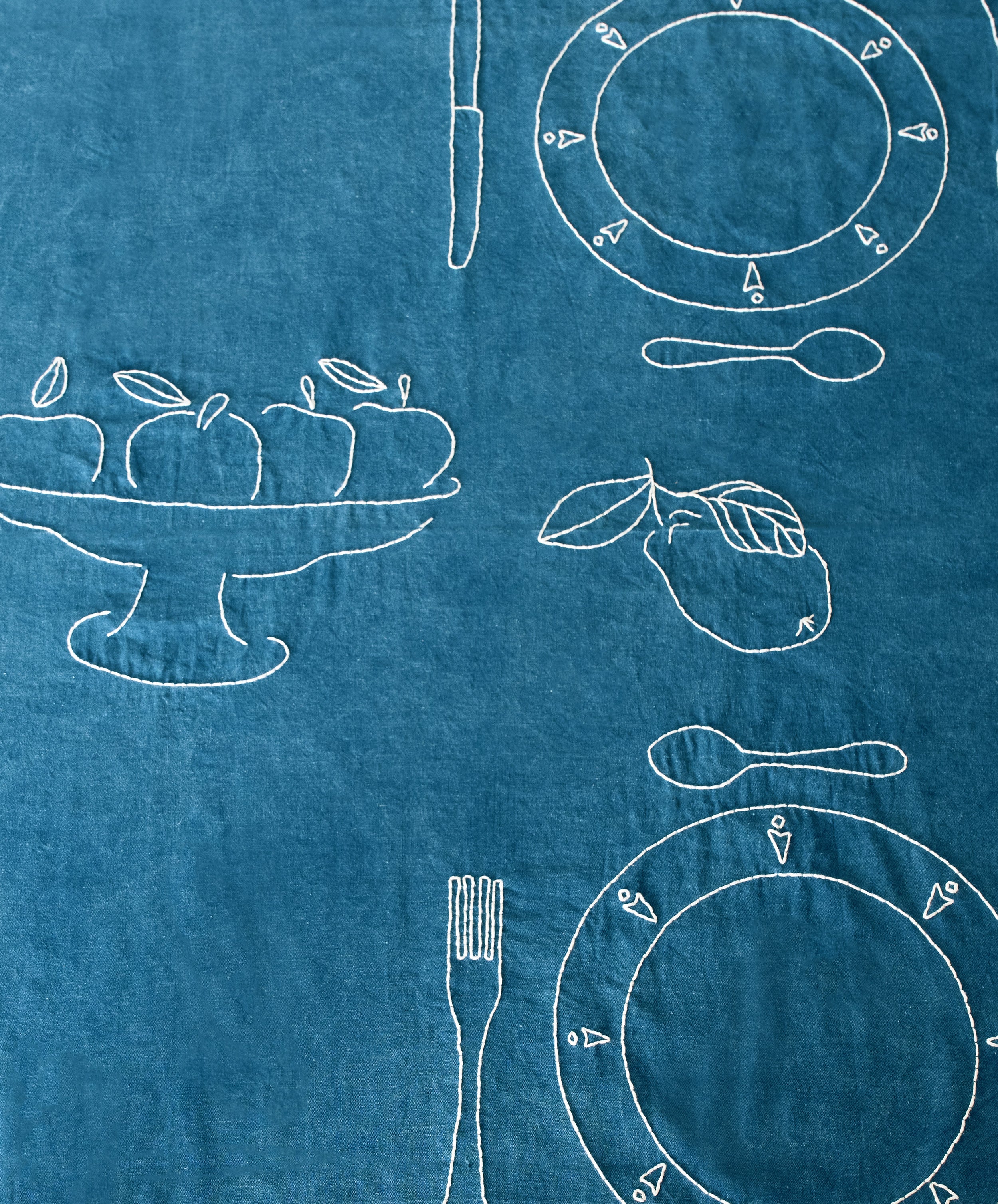 Close-up of white thread-embroidered fruit and table settings on Dîner d'Eté tablecloth in indigo linen.