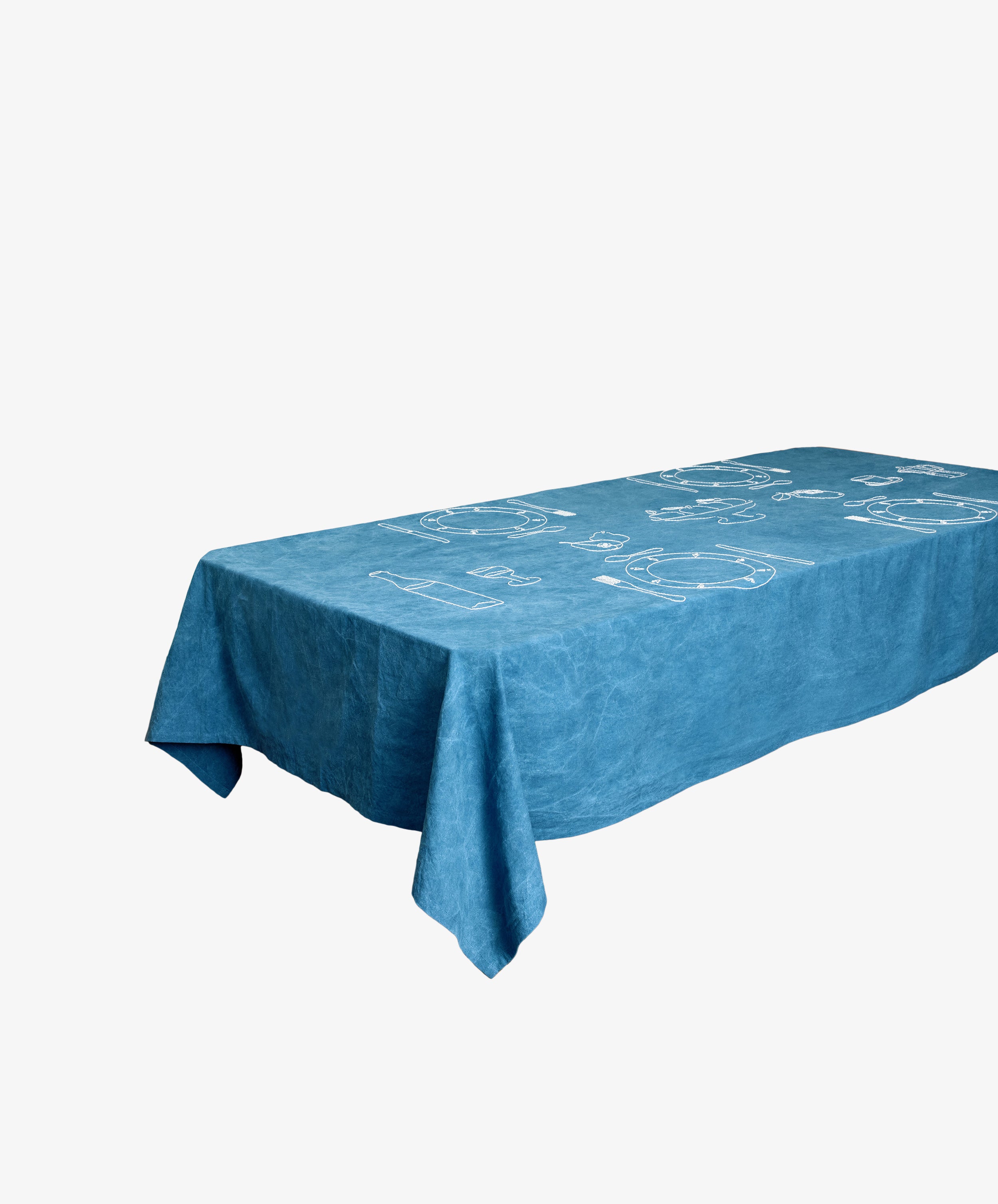 A rectangular table draped with the Dîner d'Eté custom tablecloth—blue vintage linen featuring simple white line drawings—isolated on a white background.