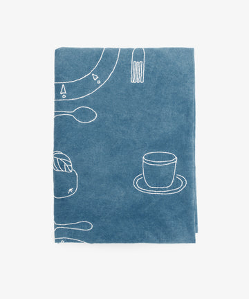 The Dejeuner d'Eta Custom Tablecloth features a blue fabric with white line drawings of coffee cups, saucers, spoons, forks, and other tableware, evoking the charm of vintage linens.