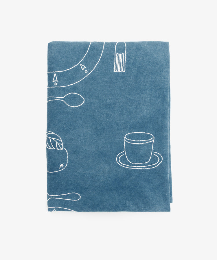 The Dejeuner d'Eta Custom Tablecloth features a blue fabric with white line drawings of coffee cups, saucers, spoons, forks, and other tableware, evoking the charm of vintage linens.