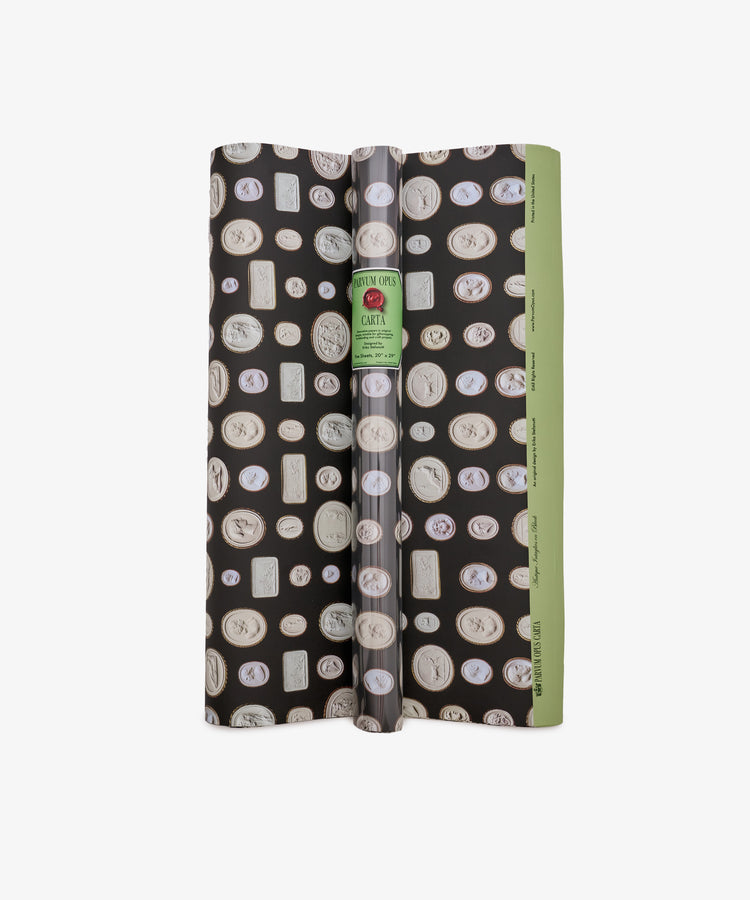 A roll of Intaglio Gift Wrap featuring a black and green design with assorted cameo-style medallions inspired by engraved gems, finished with a white label reading Carter—perfect for Grand Tour gifts.