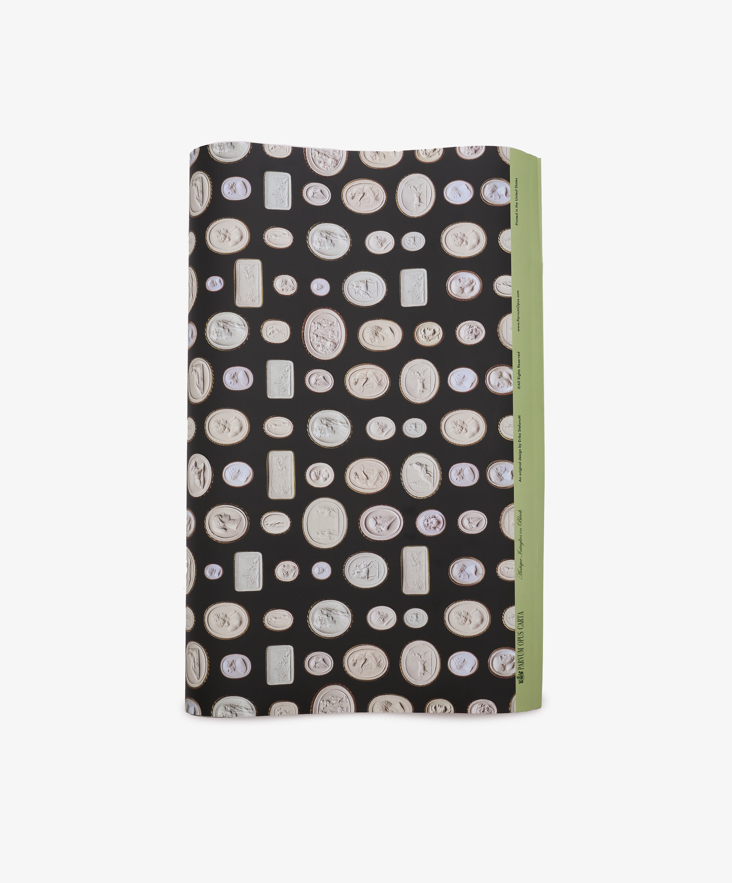 A rectangular object wrapped in Intaglio Gift Wrap, featuring black paper decorated with white coin-like motifs and accented by a green edge on the right, reminiscent of the luxurious packages used for Grand Tour gifts.