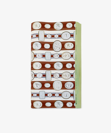 Intaglio Stripe Gift Wrap features folded paper with white coins and medallions on brown and white horizontal stripes, accented by a green border—perfect for neoclassical gift wrap enthusiasts inspired by Parvum Opus.