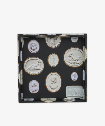 The Intaglio Nesting Tray is a square tray with a black background, showcasing finely detailed classical carved cameo and cameo-style relief designs in white and gold tones. Crafted from archival book board, this elegant scholar desk accessory combines refined artistry with functional sophistication.