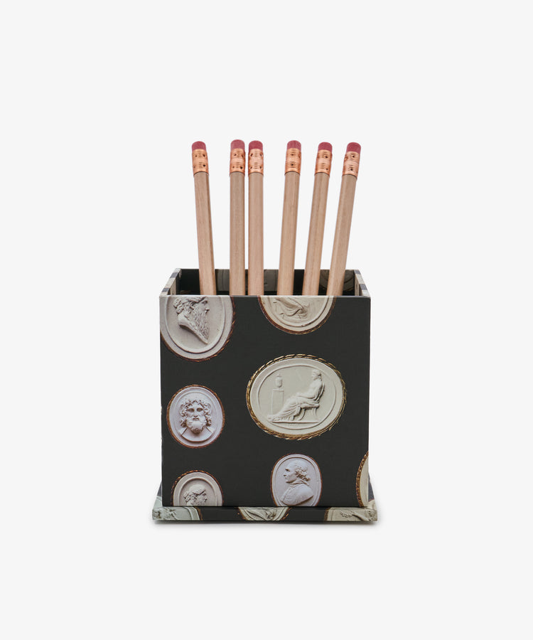 The Intaglio Pencil Pot, featuring classical carved designs in black, holds six wooden pencils with pink erasers, displayed against a white background.