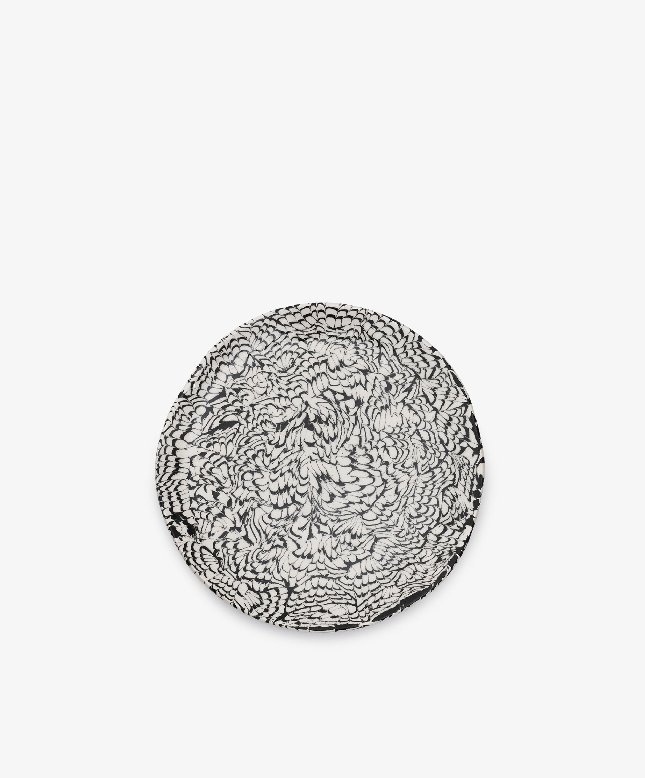 The Celine Serving Plate is a round ceramic piece, handcrafted with a striking black and white abstract, feather-like pattern reminiscent of classic Aptware designs, set against a plain white background.