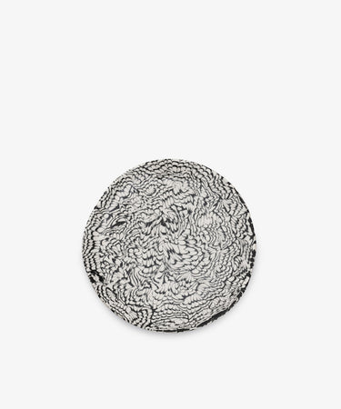 The Celine Serving Plate is a round ceramic piece, handcrafted with a striking black and white abstract, feather-like pattern reminiscent of classic Aptware designs, set against a plain white background.