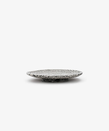The Celine Serving Plate, a low, round, handcrafted silver dish with a textured, patterned surface, sits on a plain white background.