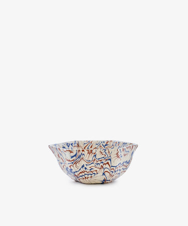 The Celine Snack Bowl is a marbled ceramic piece with a wavy rim, showcasing a red and blue abstract pattern on a white background, displayed against a plain white backdrop.