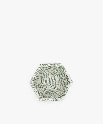 The Celine Snack Bowl is a small hexagonal dish inspired by aptware, showcasing a green and white swirling feather-like pattern centered on a crisp white background.