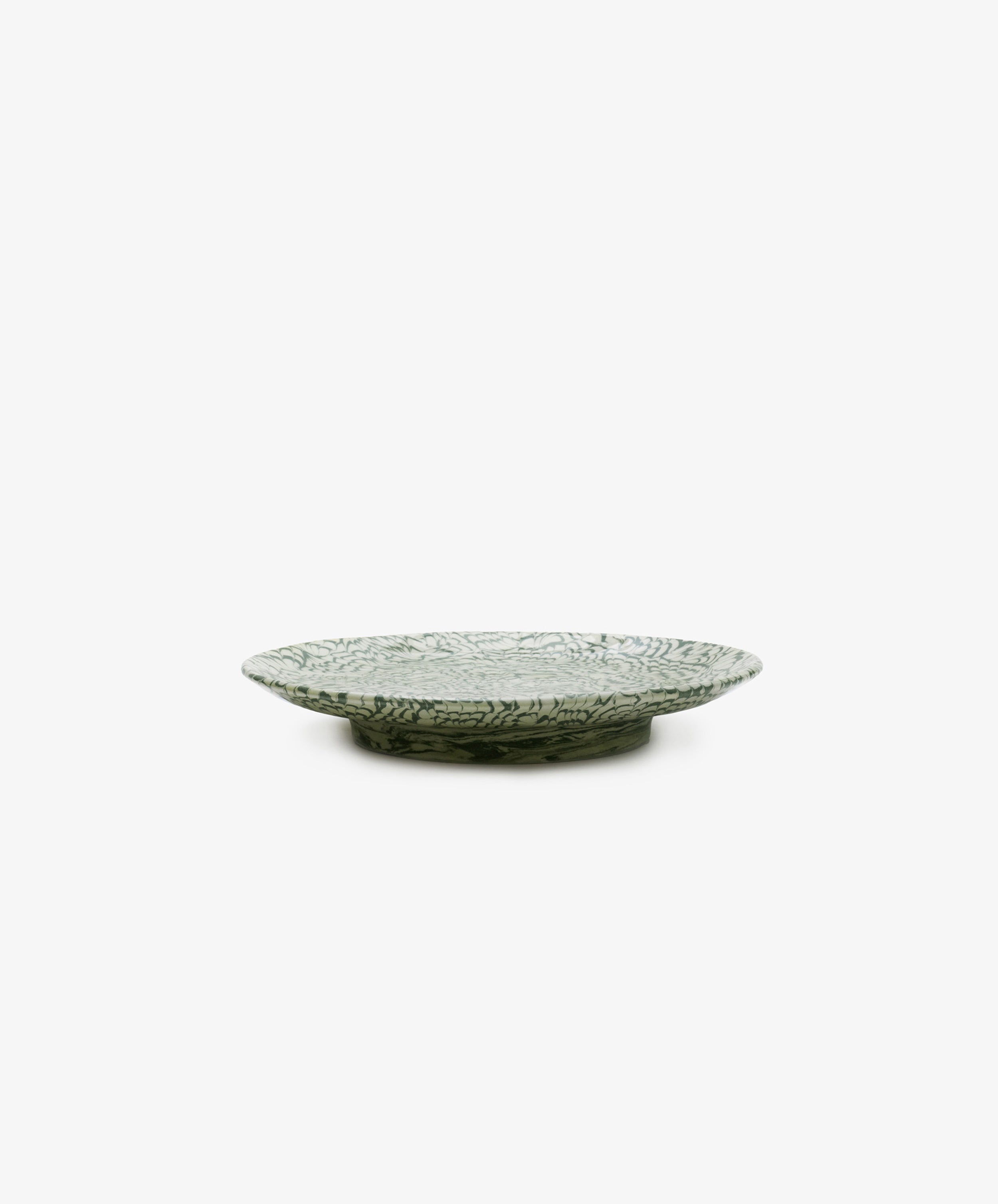 The Celine Serving Plate, a handcrafted shallow and round ceramic platter featuring a green and white leaf pattern, is elegantly displayed on a white background.