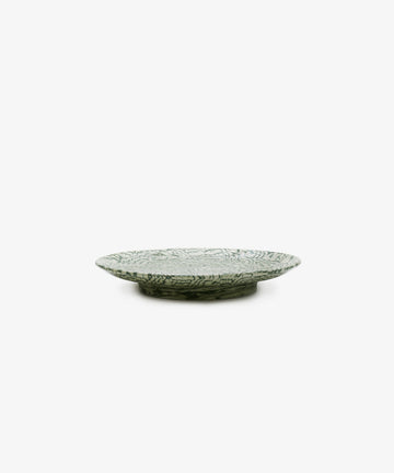 The Celine Serving Plate, a handcrafted shallow and round ceramic platter featuring a green and white leaf pattern, is elegantly displayed on a white background.