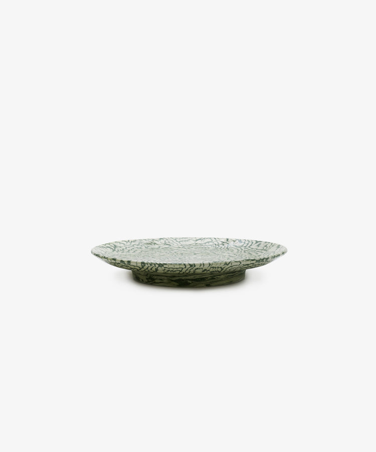 The Celine Serving Plate, a handcrafted shallow and round ceramic platter featuring a green and white leaf pattern, is elegantly displayed on a white background.