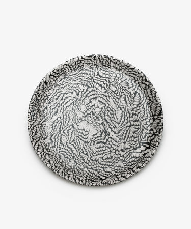 The Celine Serving Platter is a handcrafted round ceramic plate featuring an intricate black and white feather-like pattern on a plain white background.