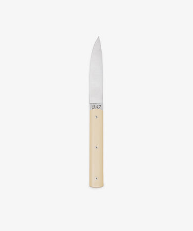The 9.47 Table Knife features a straight, pointed steel blade and a smooth, light-colored handle, displayed against a white background to highlight its French craftsmanship inspired by the iconic Perceval 9.47.