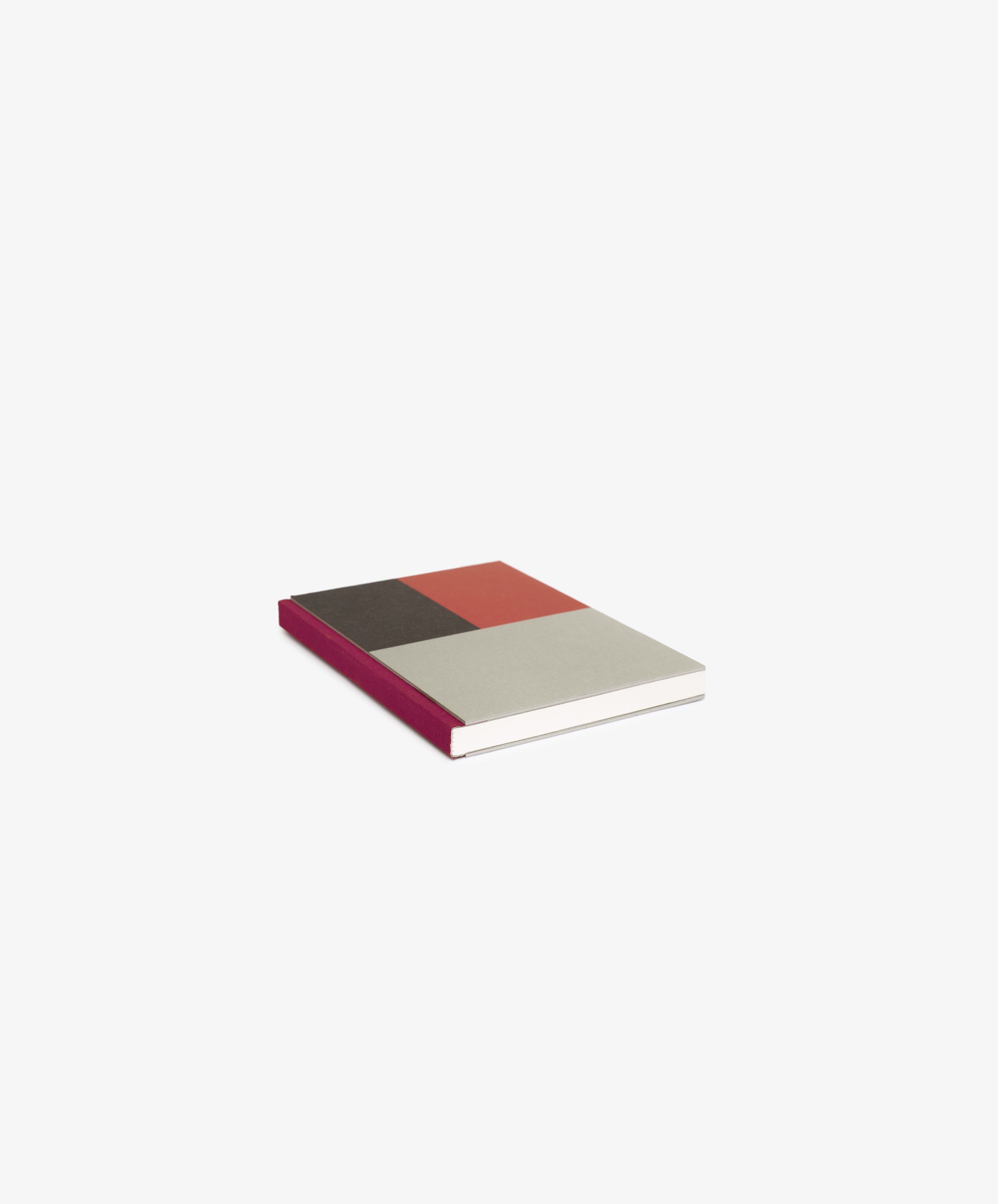 The Dreamer's Notebook, featuring a closed multicolored cover with gray, brown, and red sections plus a burgundy spine, rests on a white background—ideal for jotting down thoughts or notes.