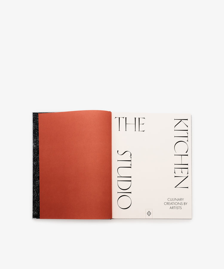 An open book reveals a red left page and a right title page featuring The Kitchen Studio: Culinary Creations by Artists in bold black text—an inventive cookbook that highlights creative recipes and the artistic visions of contemporary creators.