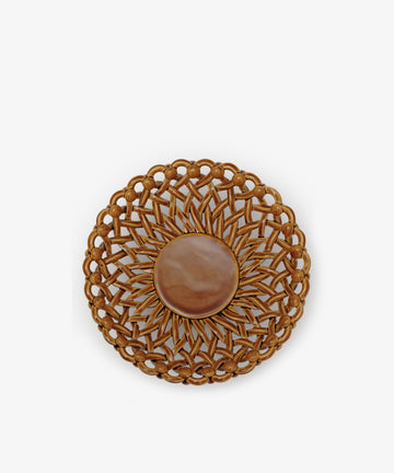 The Remi Footed Bowl features a round woven rattan design with a sunburst pattern and a solid center, echoing sculptural elements of Remi decor, and is shown against a white background.