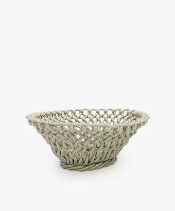 The Remi Decorative Fruit Bowl is a round, shallow woven basket with an open lattice design, evoking the charm of hand-braided clay and displayed against a plain white background.