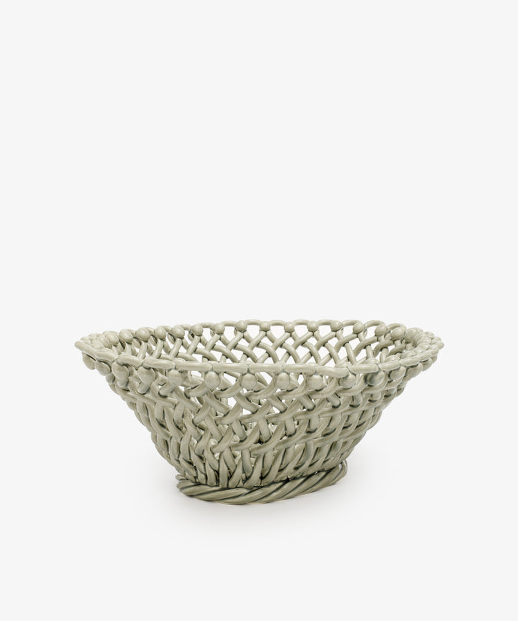 The Remi Decorative Fruit Bowl is a round, shallow woven basket with an open lattice design, evoking the charm of hand-braided clay and displayed against a plain white background.