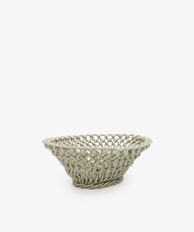 The Remi Decorative Fruit Bowl is a shallow, round woven basket in a light hue, perfect for displaying fruit or adding an artistic touch to any room. Shown on a plain white background.