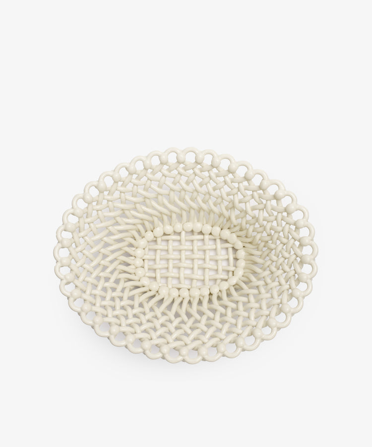 The Remi Decorative Fruit Bowl is an oval, cream-glazed ceramic basket with an open-weave design and scalloped edges, crafted by hand-braiding clay. Perfect as a decorative fruit bowl, it is shown against a plain white background.