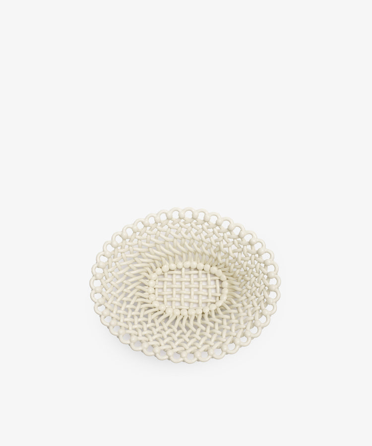 The Remi Decorative Fruit Bowl is a round, off-white woven basket tray featuring a textured pattern and open lattice design, inspired by South of France craftsmanship, shown on a plain white background.