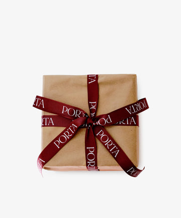Gift Wrapping: A box wrapped in plain brown paper and tied with a burgundy PORTA-printed ribbon, displayed against a white background.