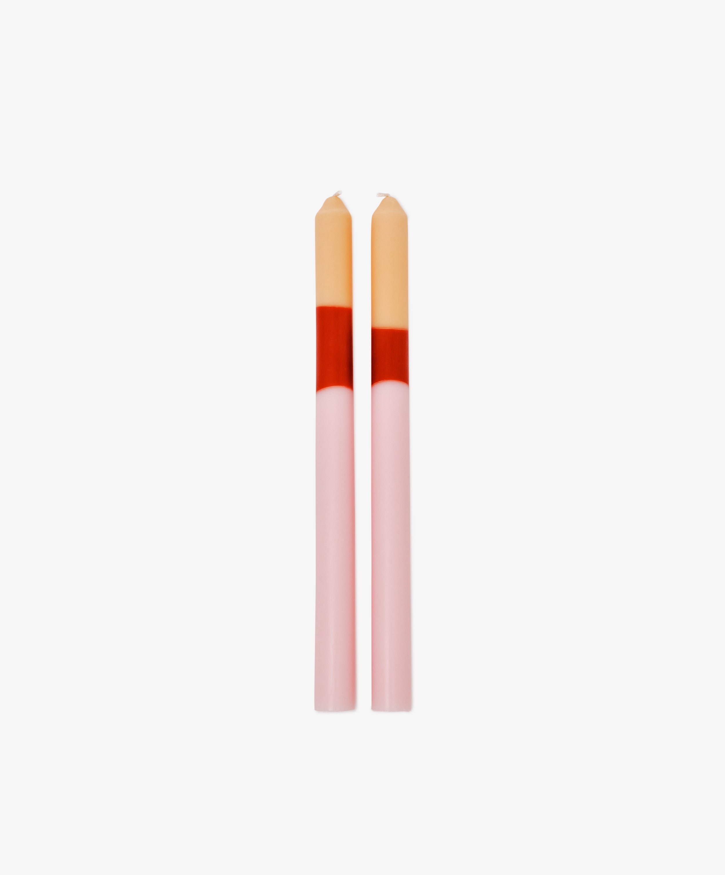 The Deia Candle set features two pink taper sculptural candles with red and beige color blocks at the top, standing side by side against a white background for unique table decor.