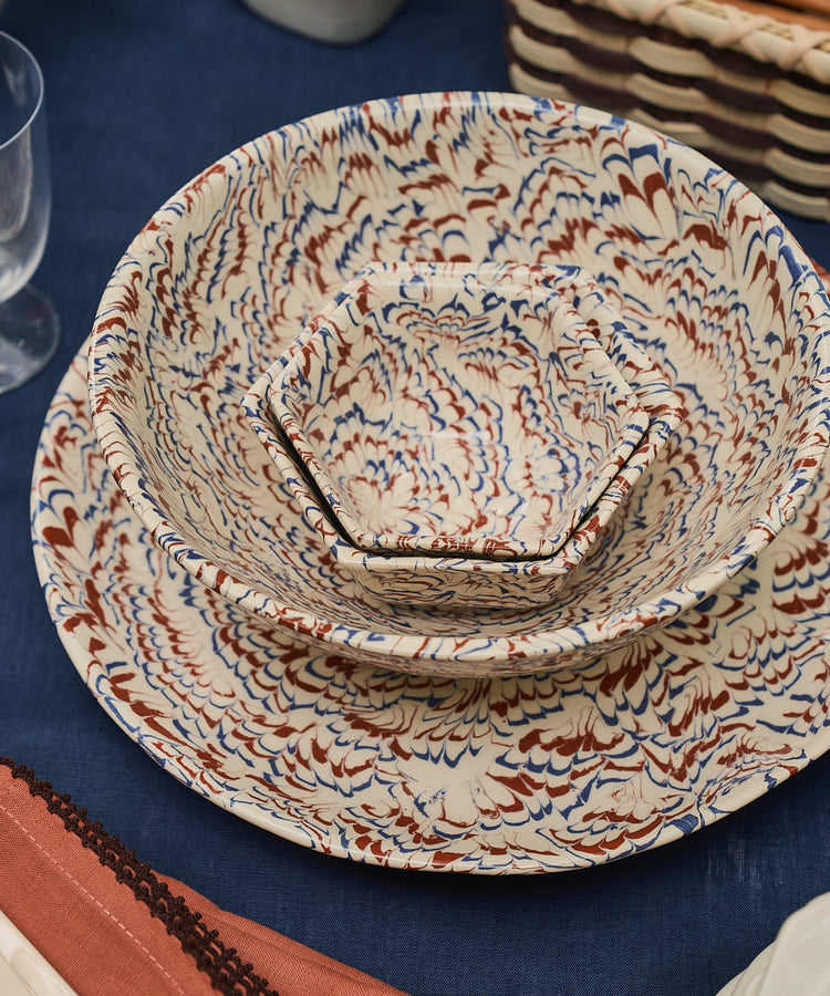 Three ceramic Celine Snack Bowls with marbled patterns are stacked on a blue tablecloth, next to glassware, cutlery, and a basket—evoking the timeless charm of classic Aptware, perfect for serving as elegant aperitivo bowls.