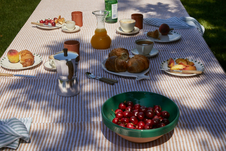 Outdoor table set with pastries, cherries, juice, and coffee on a striped tablecloth.