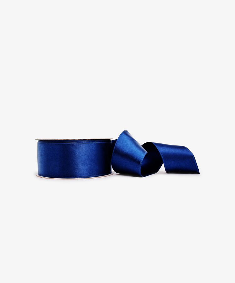A roll of Double Faced Satin Ribbon in dark blue, with a loose end extending right on a plain white background—ideal for elegant gift wrapping.