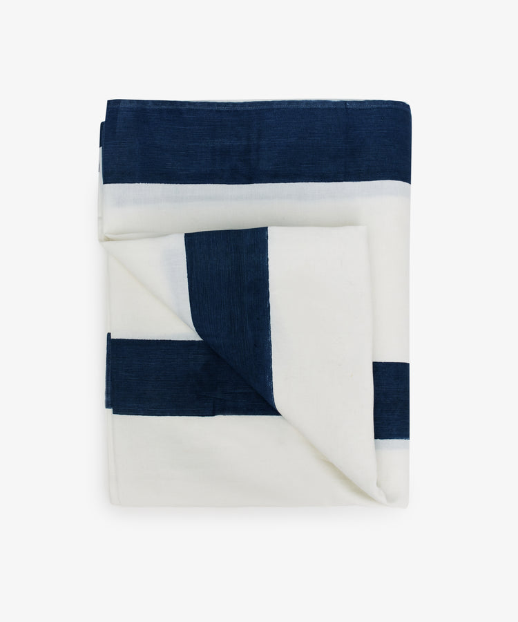 The Riga Tablecloth, an artisanal linen piece featuring wide indigo stripes, is neatly folded and displayed on a plain white background.