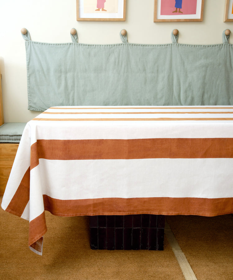 Riga Tablecloth. White linen cloth with thick rust stripes, draped on table in studio.