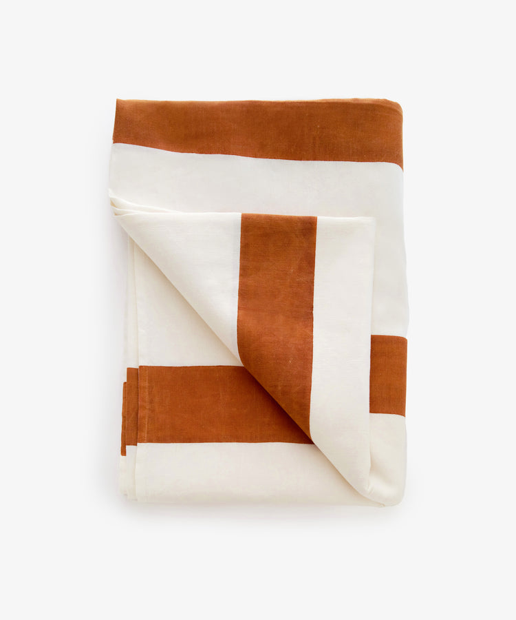 Riga tablecloth. Folded rectangular white linen cloth with thick rust stripes, with bottom corner flipped up.