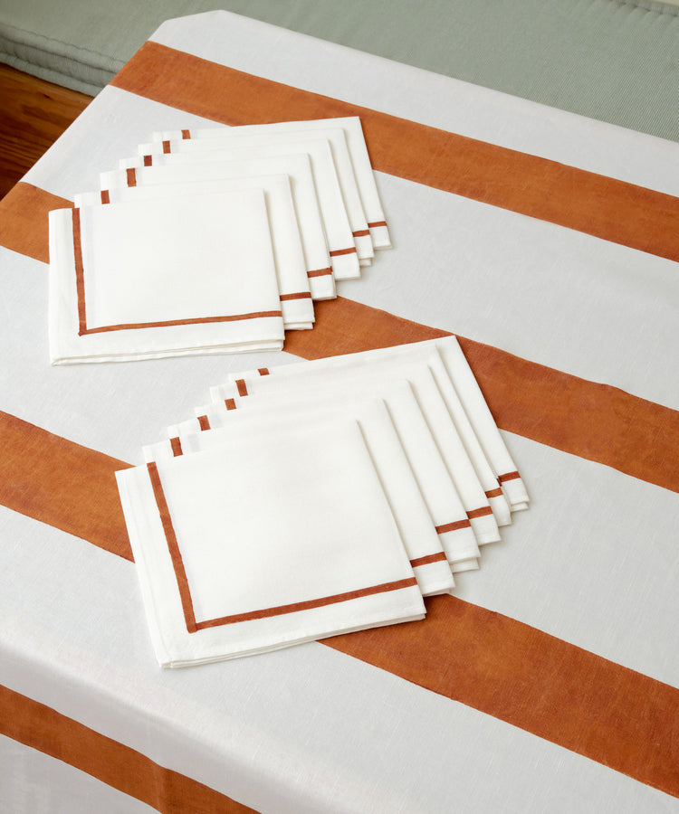 Set of white linen napkins with rust stripe detail sitting on Riga tablecloth.
