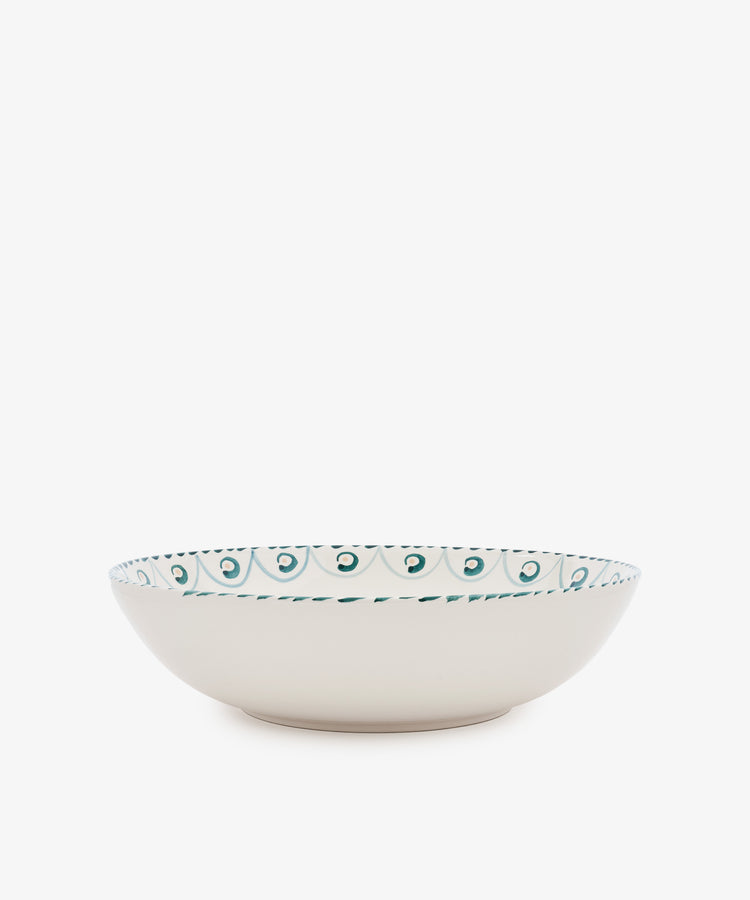 The Ottoline Serving Bowl is a shallow, cream-colored ceramic bowl with a teal and green patterned rim inspired by Tess Newall’s hand-painted designs, shown against a plain white background.