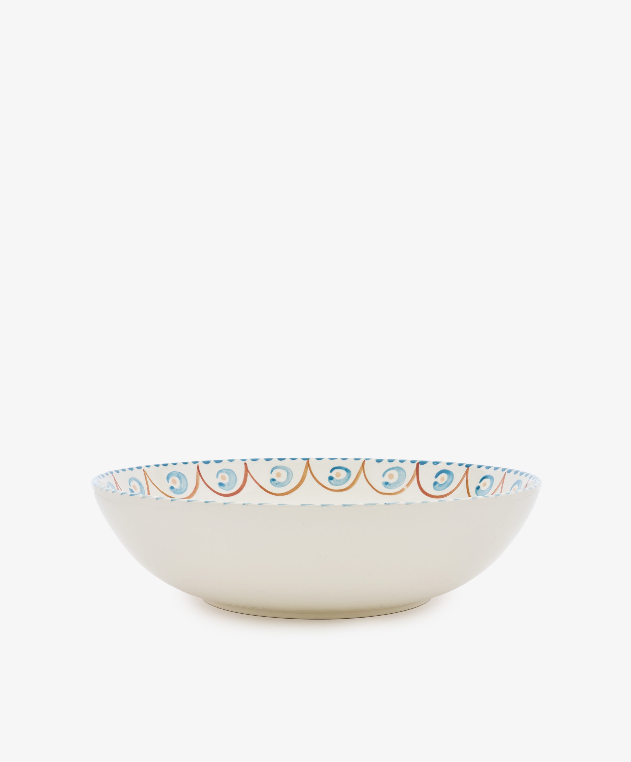 The Ottoline Serving Bowl is a shallow ceramic bowl with a cream exterior and a hand-painted blue and orange rim, evoking Italian majolica style. Shown on a white background.