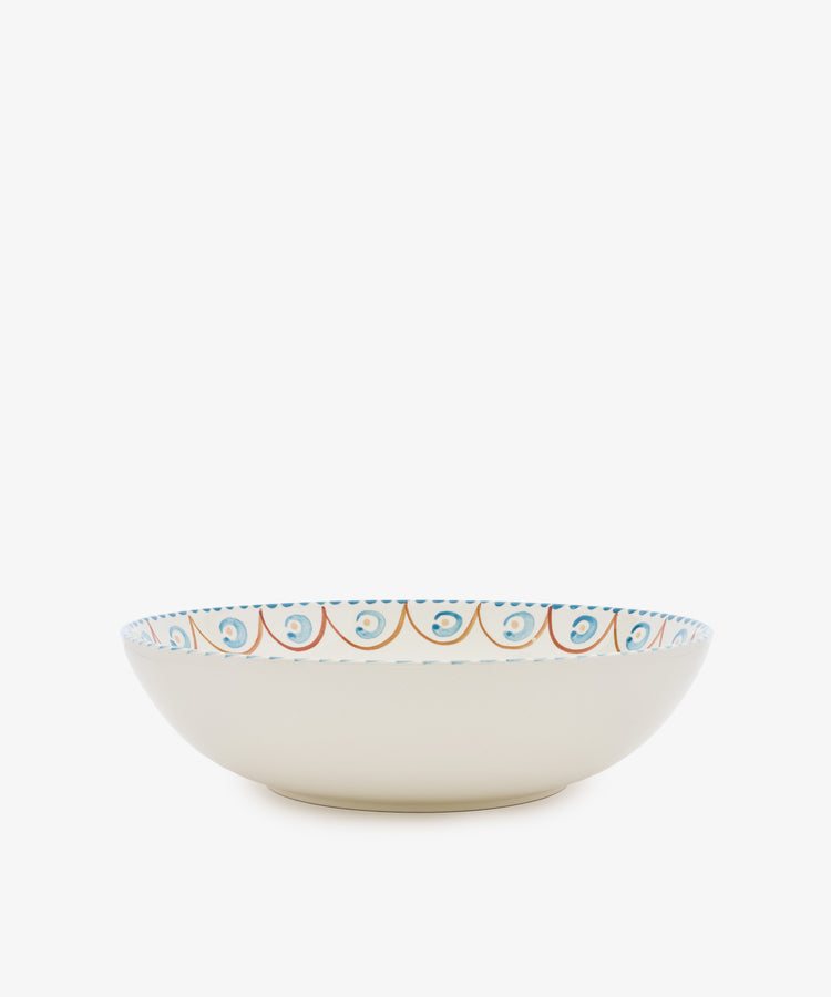 The Ottoline Serving Bowl is a shallow ceramic bowl with a cream exterior and a hand-painted blue and orange rim, evoking Italian majolica style. Shown on a white background.