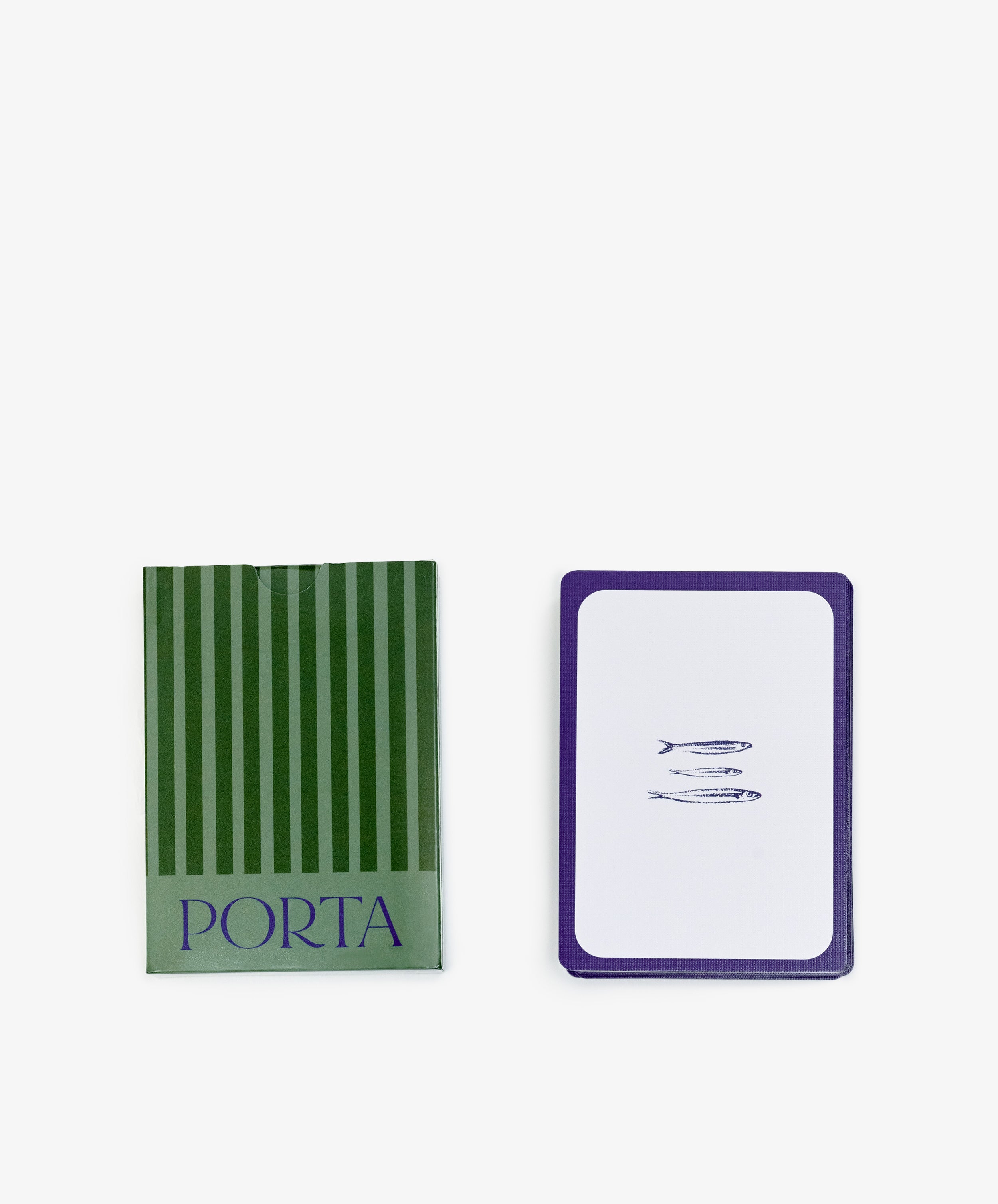 A green striped box labeled PORTA Playing Cards sits beside a stack of designer cards, with the top card displaying three small fish illustrations.