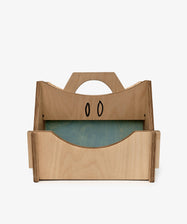 The Casper Caddy by House of RoRo is a kids wooden storage caddy with a handle, side panels, a green bottom, and two black oval designs on the back panel.