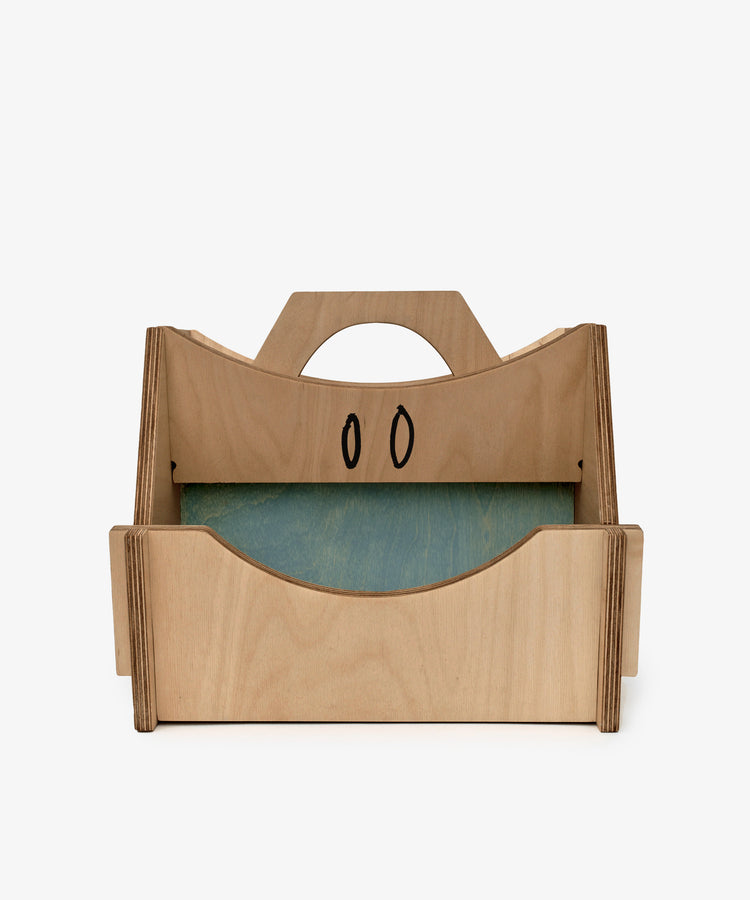 The Casper Caddy by House of RoRo is a kids wooden storage caddy with a handle, side panels, a green bottom, and two black oval designs on the back panel.