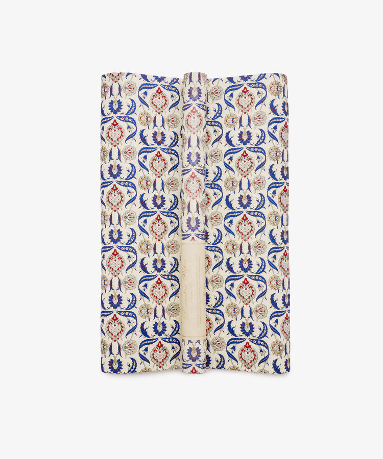 Arabesque Gift Wrap, featuring a repeating pattern of blue, red, and beige floral motifs with decorative Arabesque designs on a cream background, is displayed folded against a white surface.