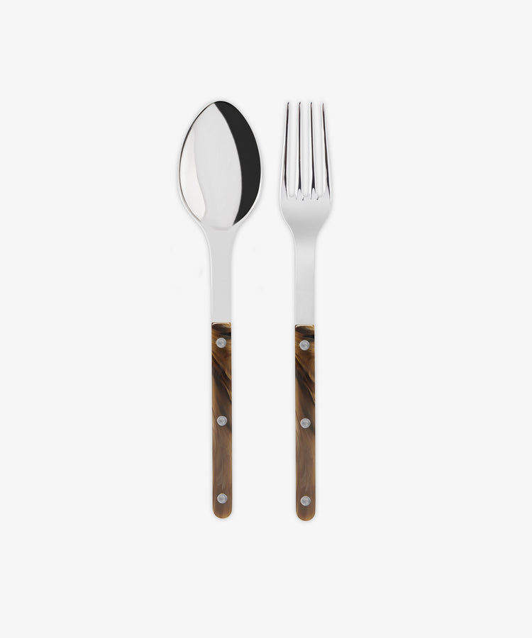 The Bistrot Serving Set features a metal spoon and fork with brown, wood-patterned handles and three rivets, side by side on a white background for a Parisian bistro look.