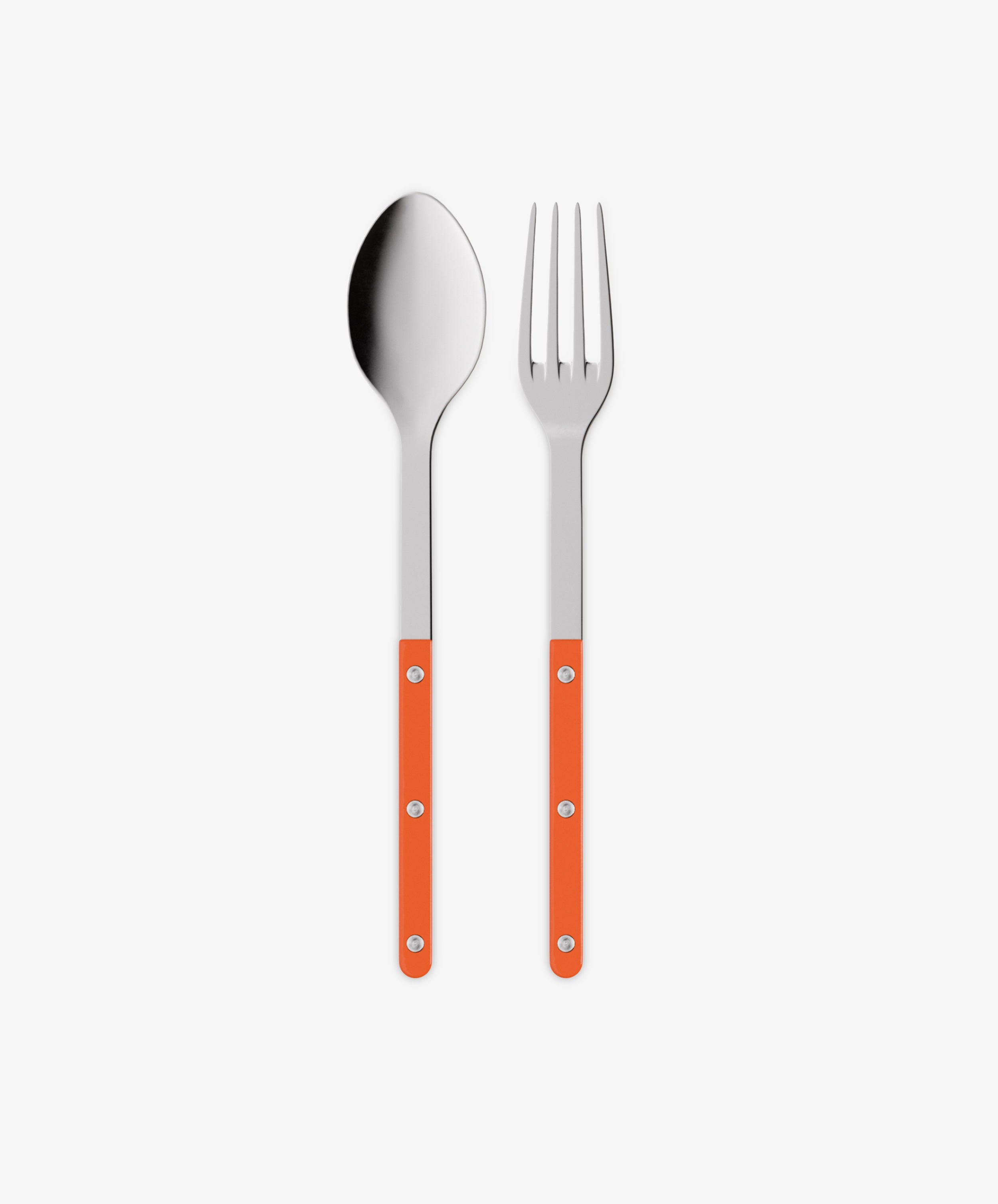The Bistrot Serving Set features a stainless steel spoon and fork with orange handles and three visible rivets, placed side by side on a white background.