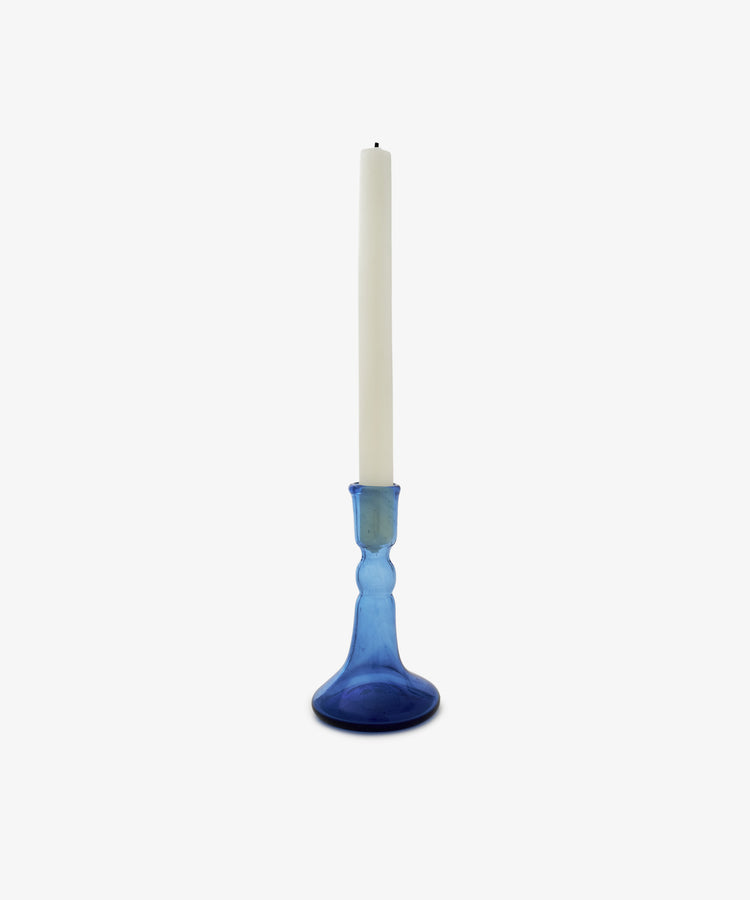 A white taper candle rests in the Lucia candleholder, made of cobalt glass, against a plain white background.