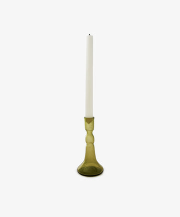 A white taper candle stands upright in the Lucia candleholder, crafted from olive glass and set against a plain white background—an elegant choice for any table setting.