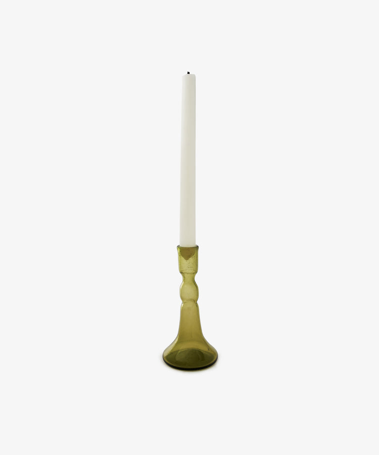 A white taper candle stands upright in the Lucia candleholder, crafted from olive glass and set against a plain white background—an elegant choice for any table setting.