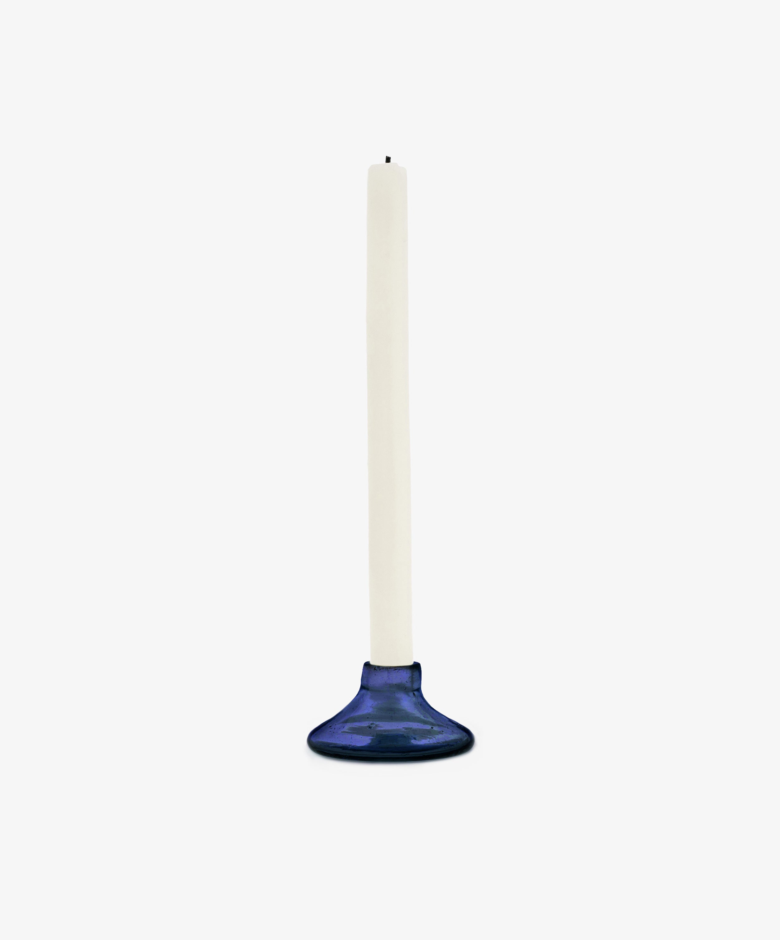 A white taper candle stands upright in the Lucien candleholder, Small—handblown in Morocco from recycled blue glass—against a plain white background.